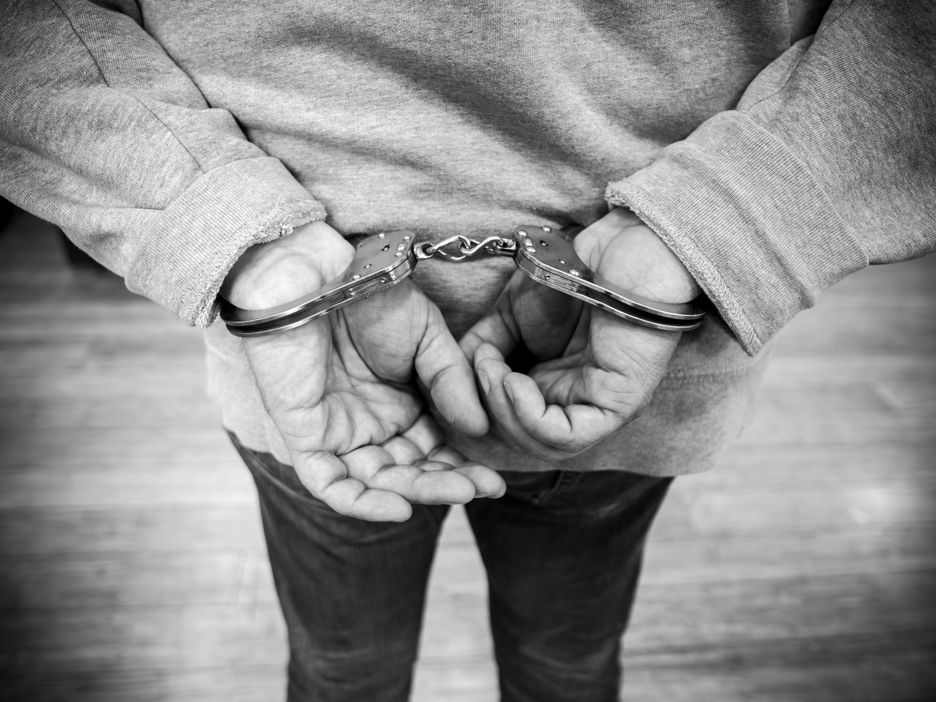 Black and white photo of a person in handcuffs, wearing a gray hoodie.