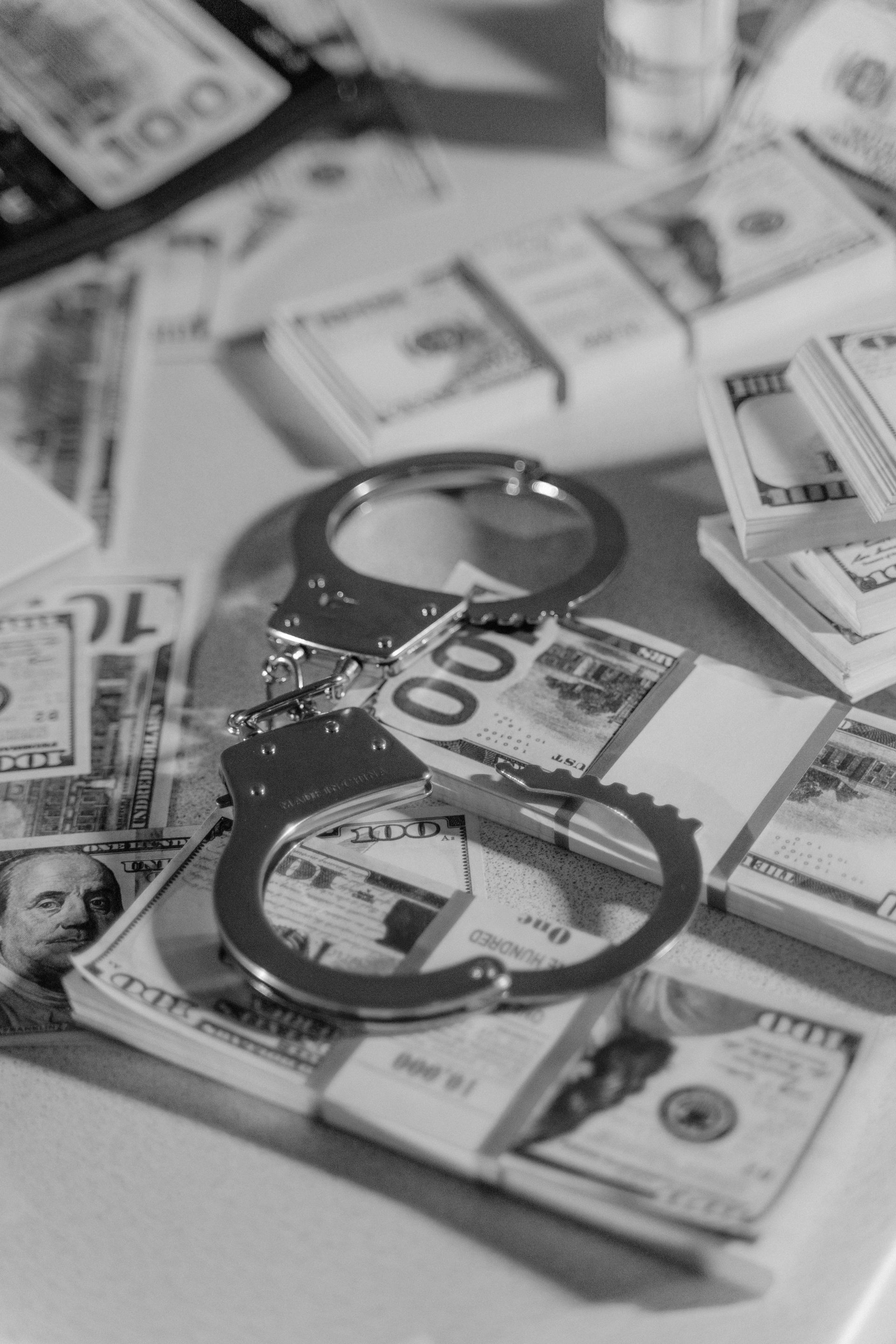 Black and white image of handcuffs placed over stacks of US dollar bills, symbolizing financial crime.